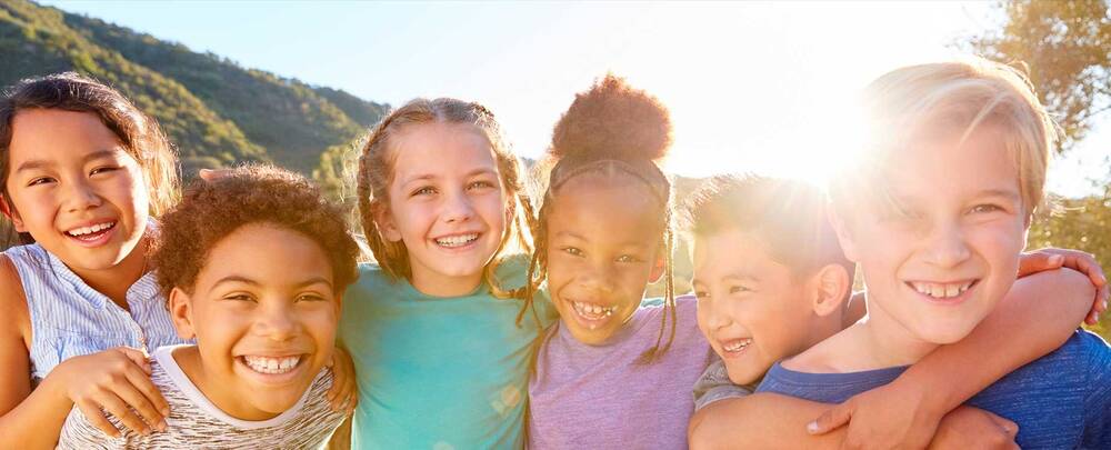 Group of children smiling with sun and hills behind them