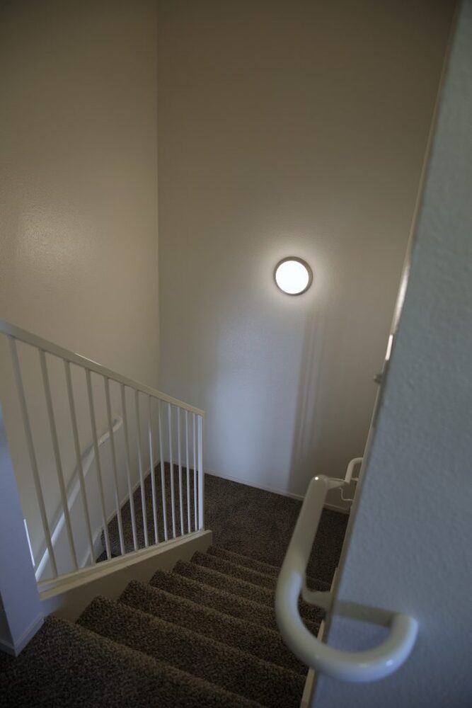 A carpeted staircase leads down, a bright round light is on the wall. 