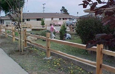 Two people doing yard work behind a wooden fence at the Guadalupe Ranch Acres.