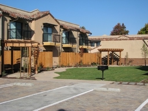 A winding sidewalk in front of the Rancho Hermosa Apartments. There is a wooden fence separating the building from the grass.